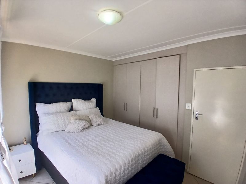 A well-maintained bedroom featuring built-in cupboards, neutral wall finishes, and a coved ceiling with a central light fixture.