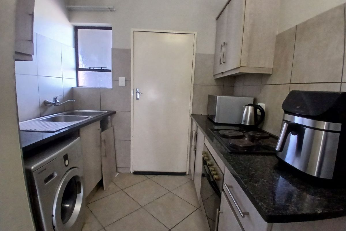 Compact kitchen featuring built-in cabinetry, granite countertops, a built-in oven, and an electric hob, with tiled flooring and backsplash throughout.
