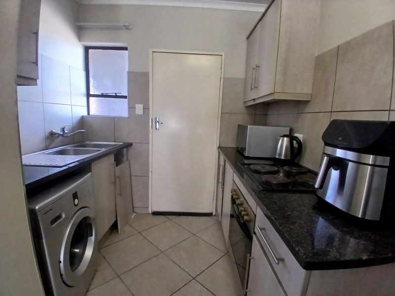 Compact kitchen featuring built-in cabinetry, granite countertops, a built-in oven, and an electric hob, with tiled flooring and backsplash throughout.