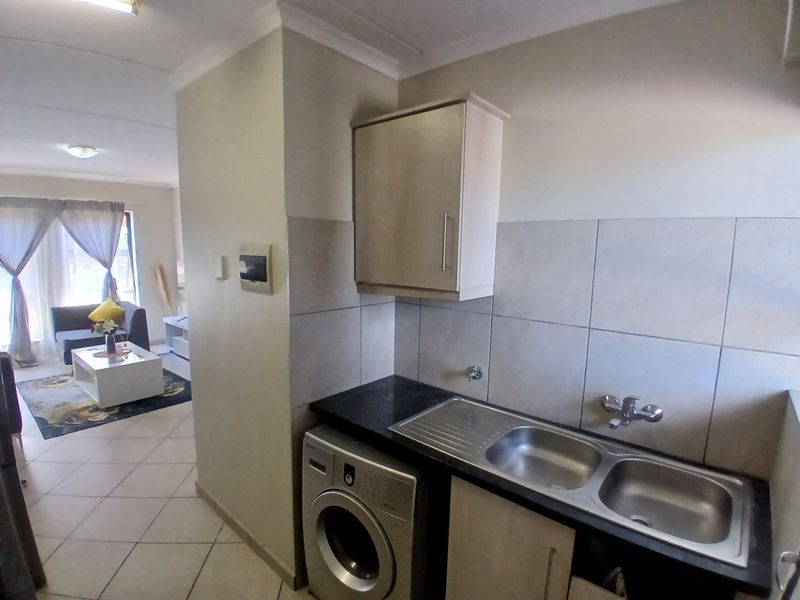 A functional scullery area featuring a double bowl stainless steel sink, granite countertops, tiled backsplash, and dedicated plumbing for a washing machine.