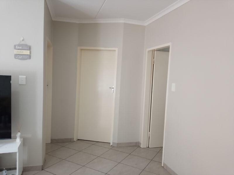 A clean and neutral hallway featuring tiled flooring, coving, and multiple internal doors leading to other areas of the apartment.