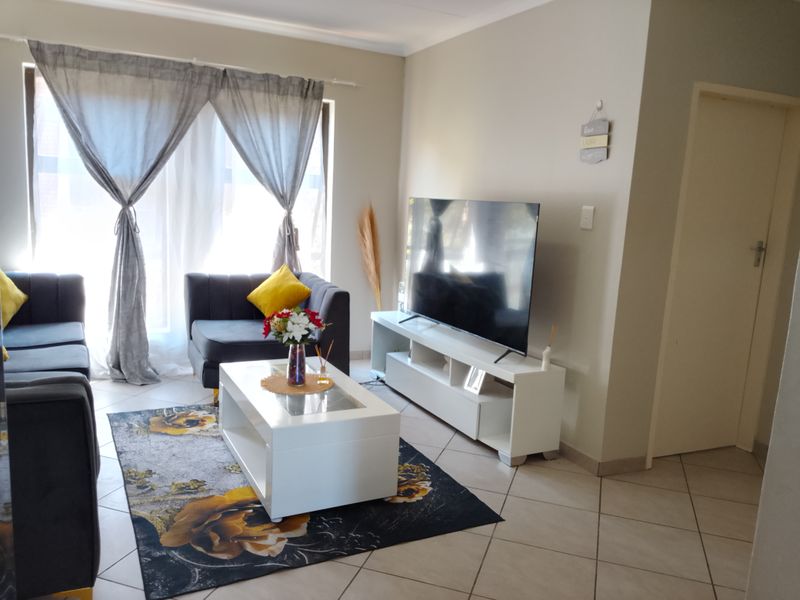 A well-maintained living room featuring neutral tiled flooring, a sliding door for natural light, and clean wall finishes.