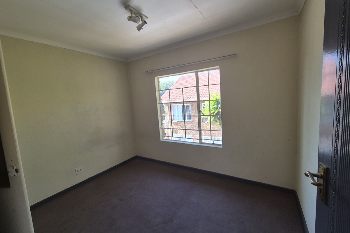 A vacant bedroom featuring carpeted flooring, a window with security bars, and a ceiling-mounted light fixture.