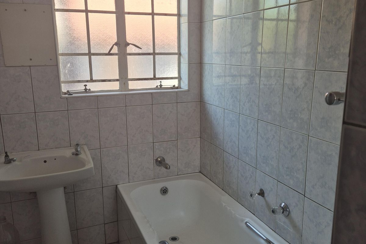 A functional bathroom featuring a white pedestal basin, a standard bathtub with chrome fixtures, and full-height wall tiling.