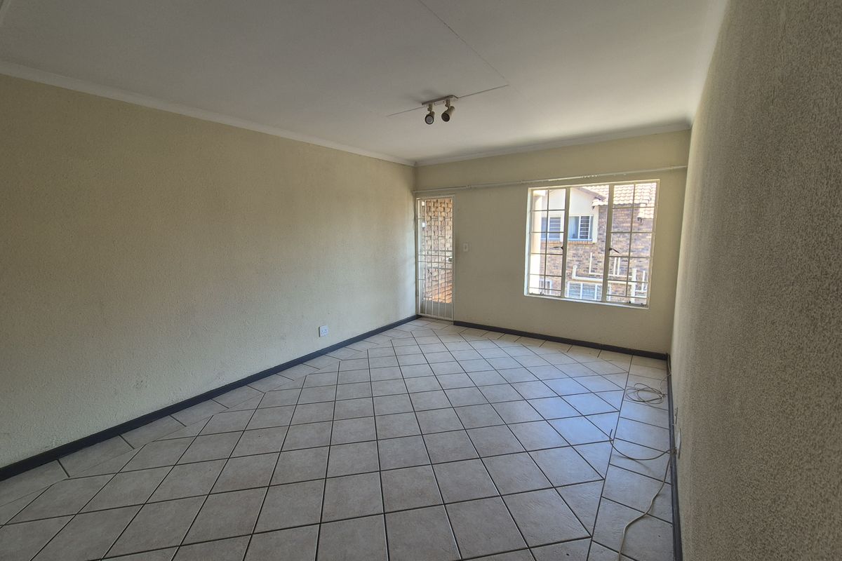 A spacious, empty living room featuring neutral tiled flooring, textured walls, and a security gate at the entrance.