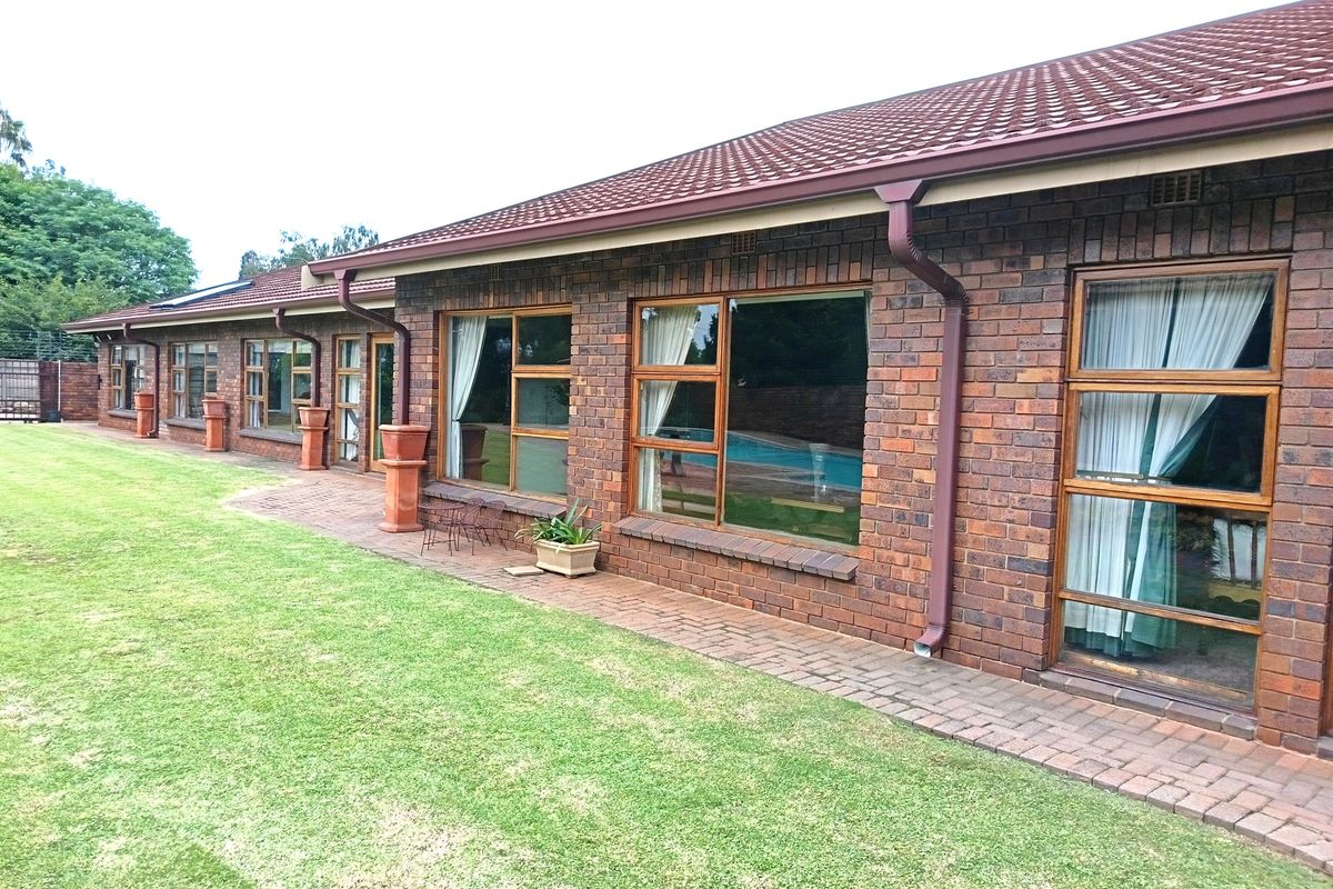 Rear view of the house featuring face-brick exterior, tiled roof, and paved walkway overlooking a well-maintained lawn and swimming pool area.