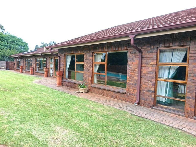 Rear view of the house featuring face-brick exterior, tiled roof, and paved walkway overlooking a well-maintained lawn and swimming pool area.