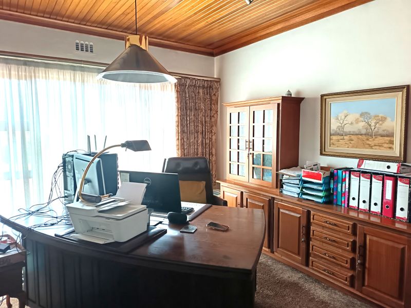 A functional home office featuring built-in timber cabinetry, a classic wood-paneled ceiling, and large windows allowing for natural light.