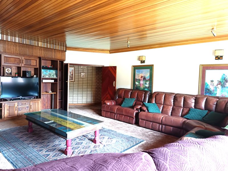 Spacious living room featuring a distinctive wood-paneled ceiling, built-in wooden cabinetry, and direct access to an adjacent room with exposed brick walls.