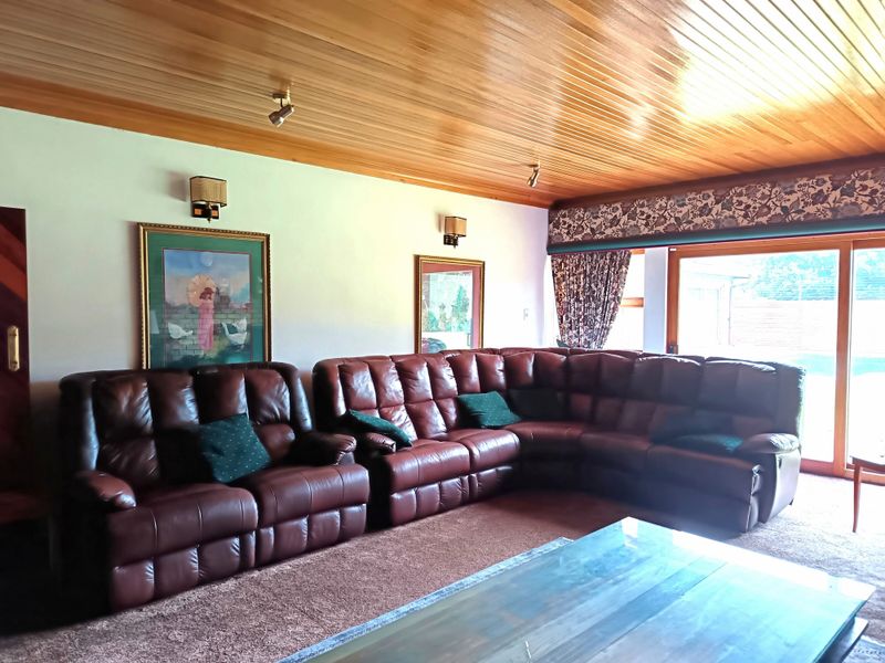 Spacious living room featuring a distinctive timber-paneled ceiling, wall-mounted lighting, and large sliding glass doors providing access to the outdoor area.