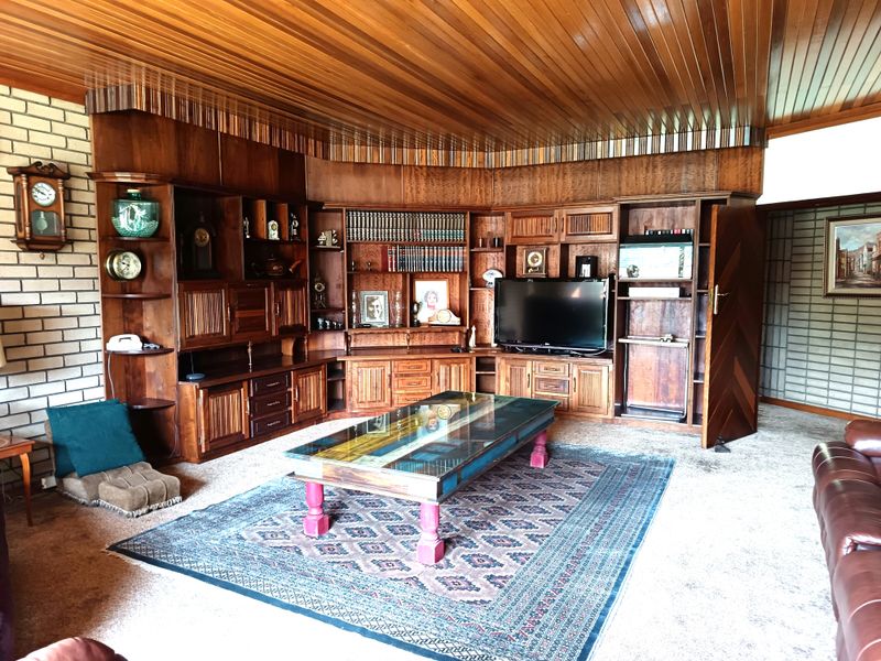 A spacious living room featuring extensive built-in wooden cabinetry, a distinctive timber-paneled ceiling, and a brick feature wall.
