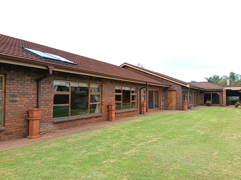 Rear view of a brick-faced house featuring a tiled roof, solar water heating panels, and large windows overlooking a well-maintained lawn.