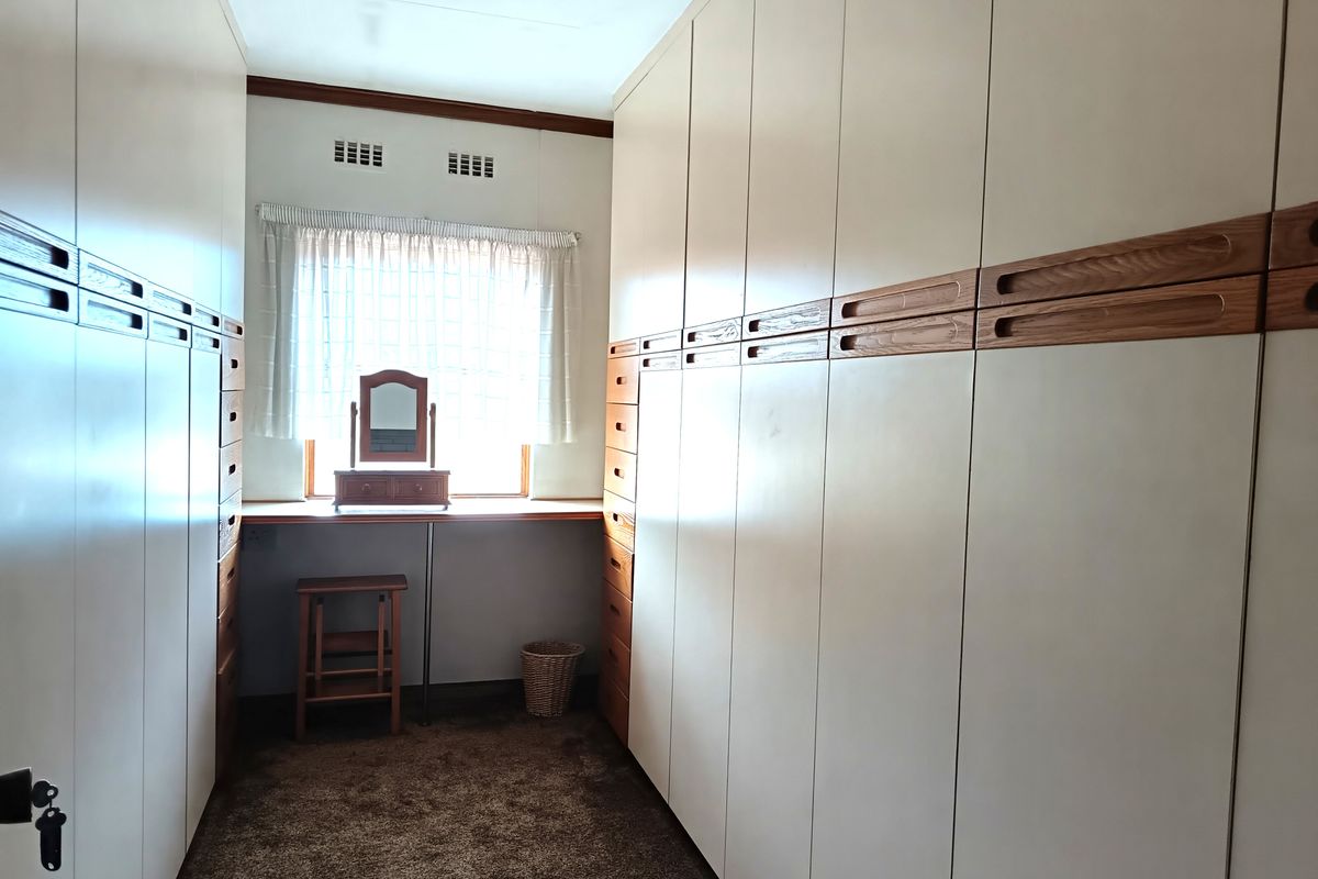 A walk-in dressing room featuring extensive floor-to-ceiling built-in cabinetry with integrated drawers and a dedicated vanity area under the window.