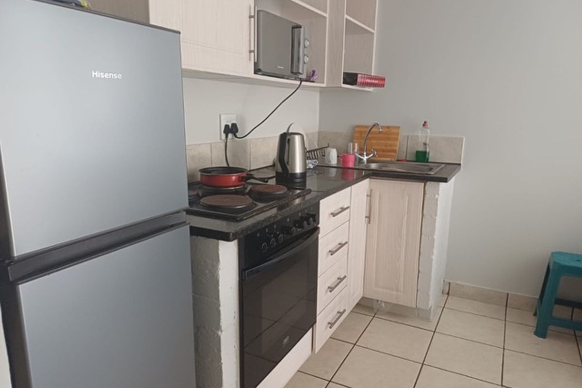 Compact kitchen featuring light-toned cabinetry, granite countertops, a built-in oven with electric hob, and tiled flooring.