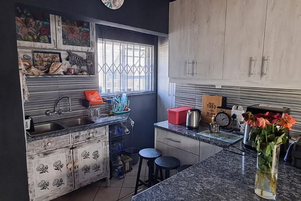 Compact kitchen featuring granite countertops, double basin sink, and ample built-in cabinetry with a tiled backsplash and security-fitted window.