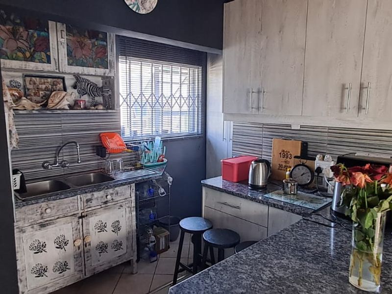 Compact kitchen featuring granite countertops, double basin sink, and ample built-in cabinetry with a tiled backsplash and security-fitted window.