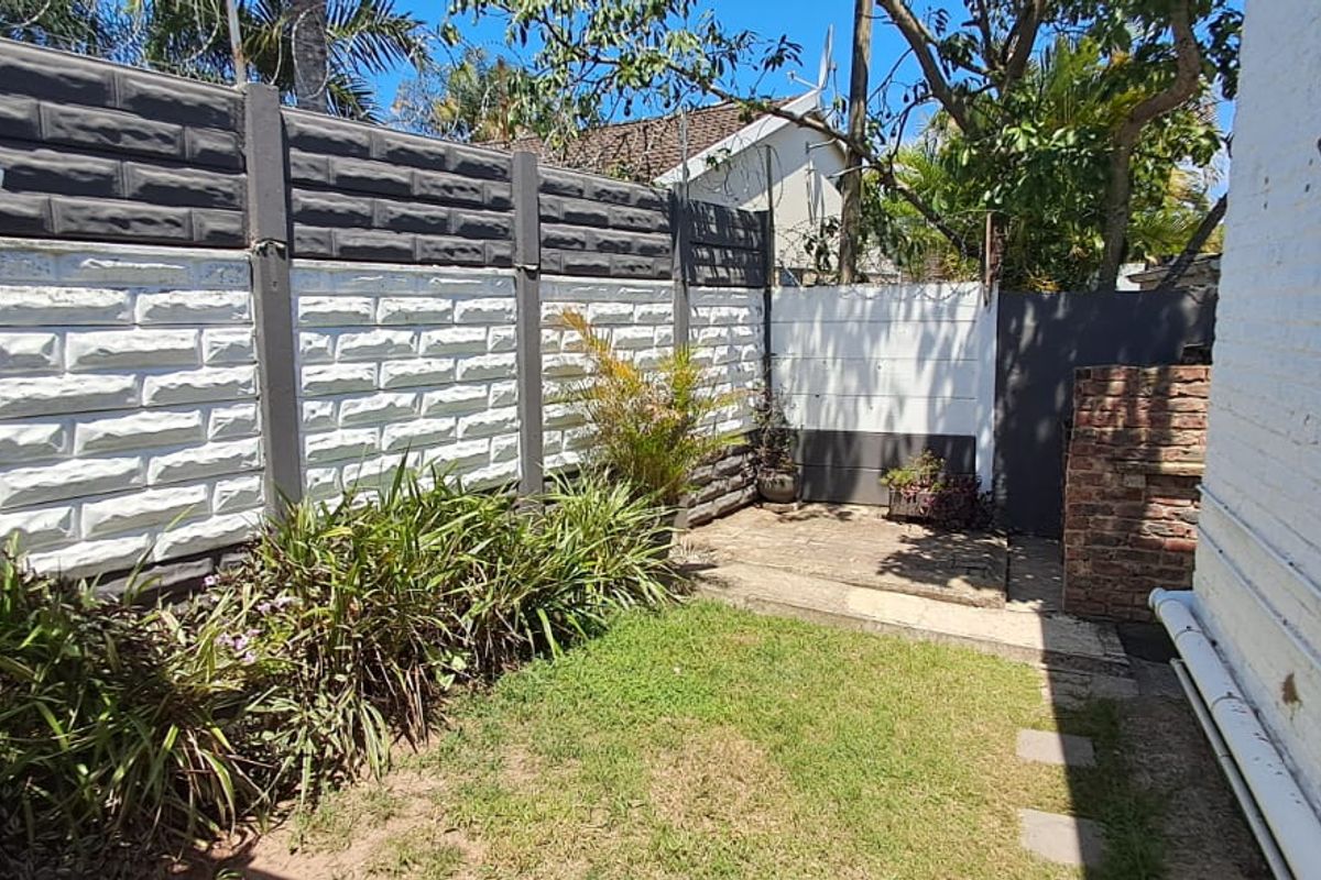 A private rear garden area featuring a precast concrete boundary wall, a small lawn, and a paved section adjacent to the building.