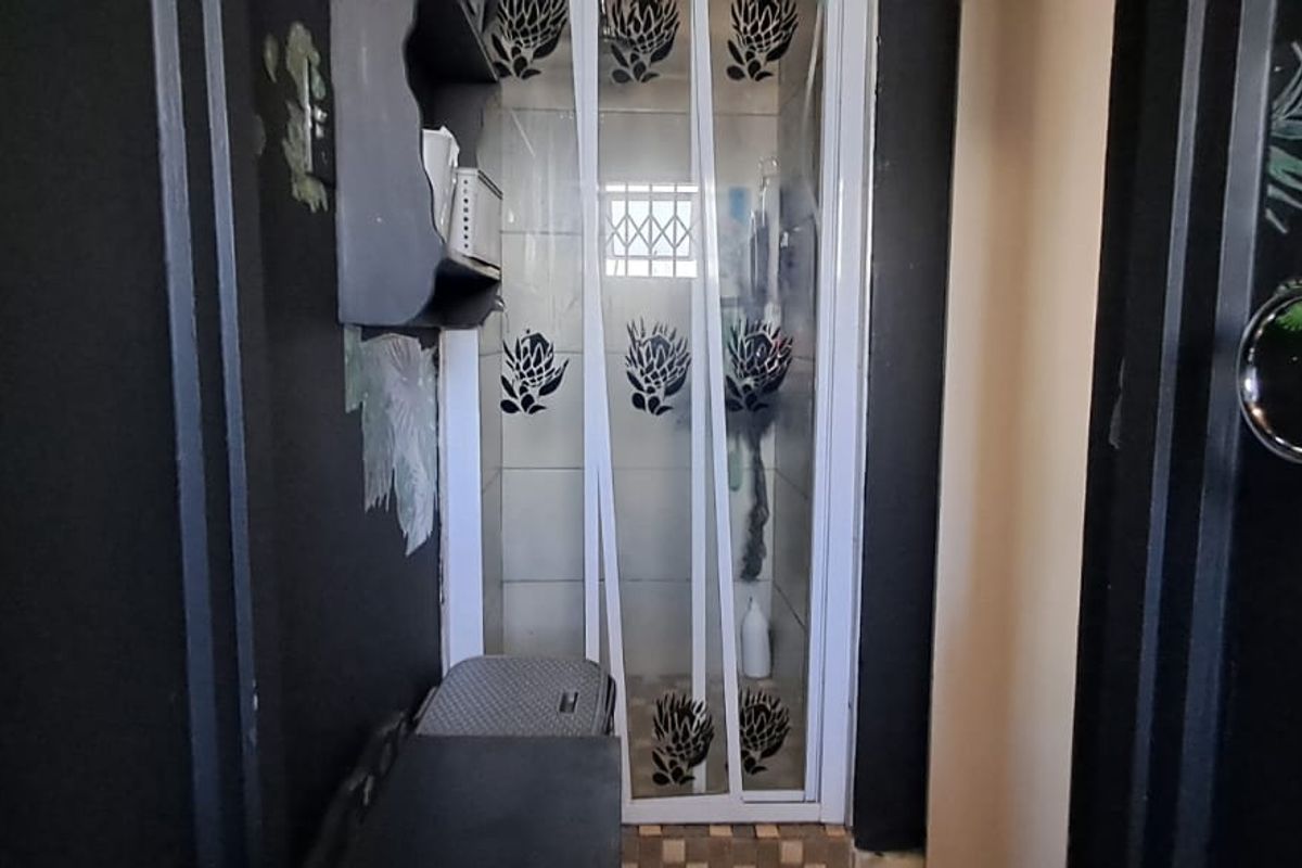 A bathroom featuring a shower enclosure with tiled walls and a towel ring, currently showing signs of wear and damage to the shower door frame.