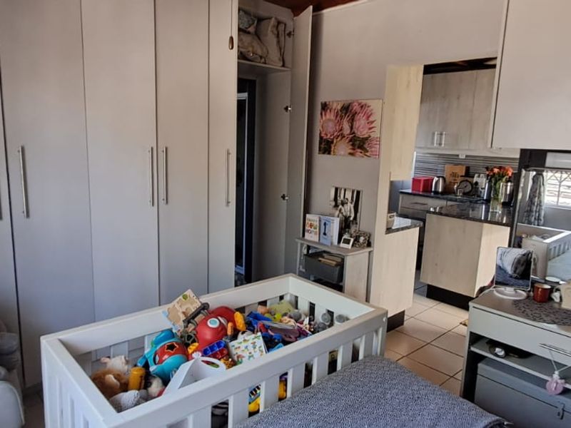 A bedroom featuring extensive built-in cupboards and a vanity unit, with tiled flooring and a view through to the adjacent kitchen area.