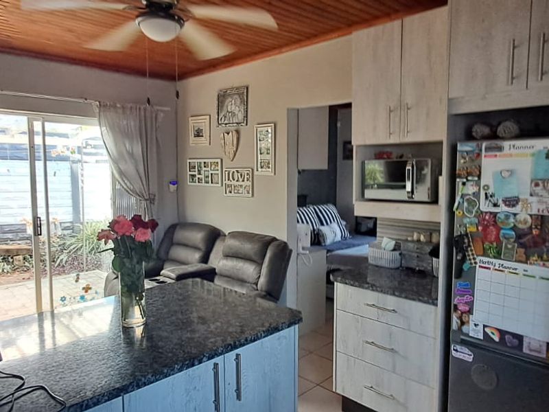 Open plan kitchen and living area featuring granite countertops, built-in cabinetry, a timber ceiling with a fan, and sliding door access to the patio.