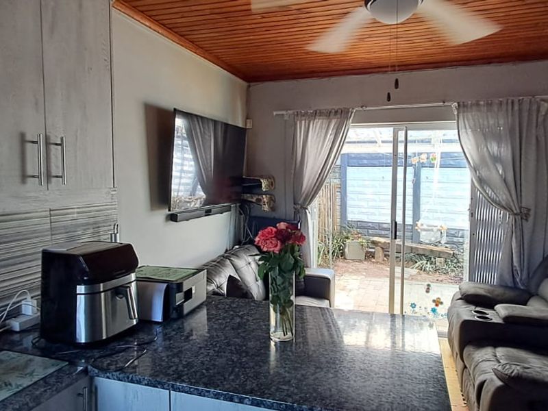 Open plan kitchen and living area featuring granite countertops, built-in cabinetry, timber ceiling, and sliding door access to the rear patio.