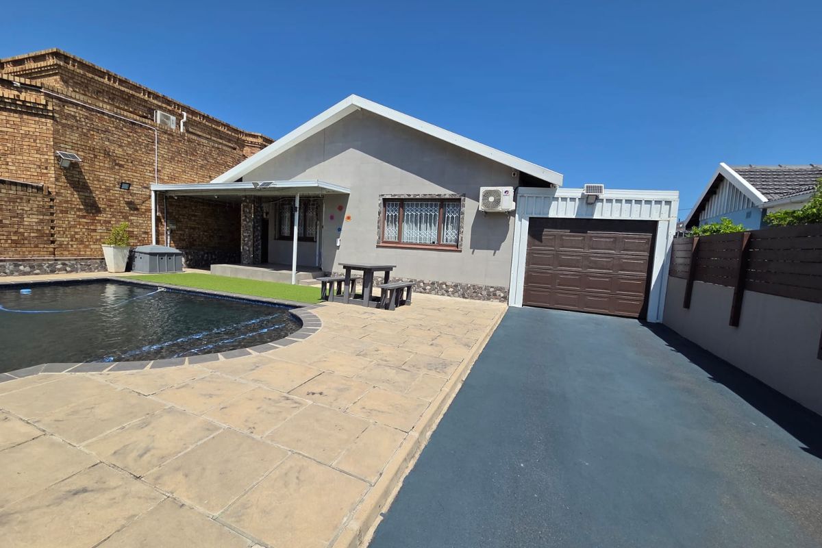 Rear exterior view featuring a swimming pool, paved patio area, attached garage, and driveway access.