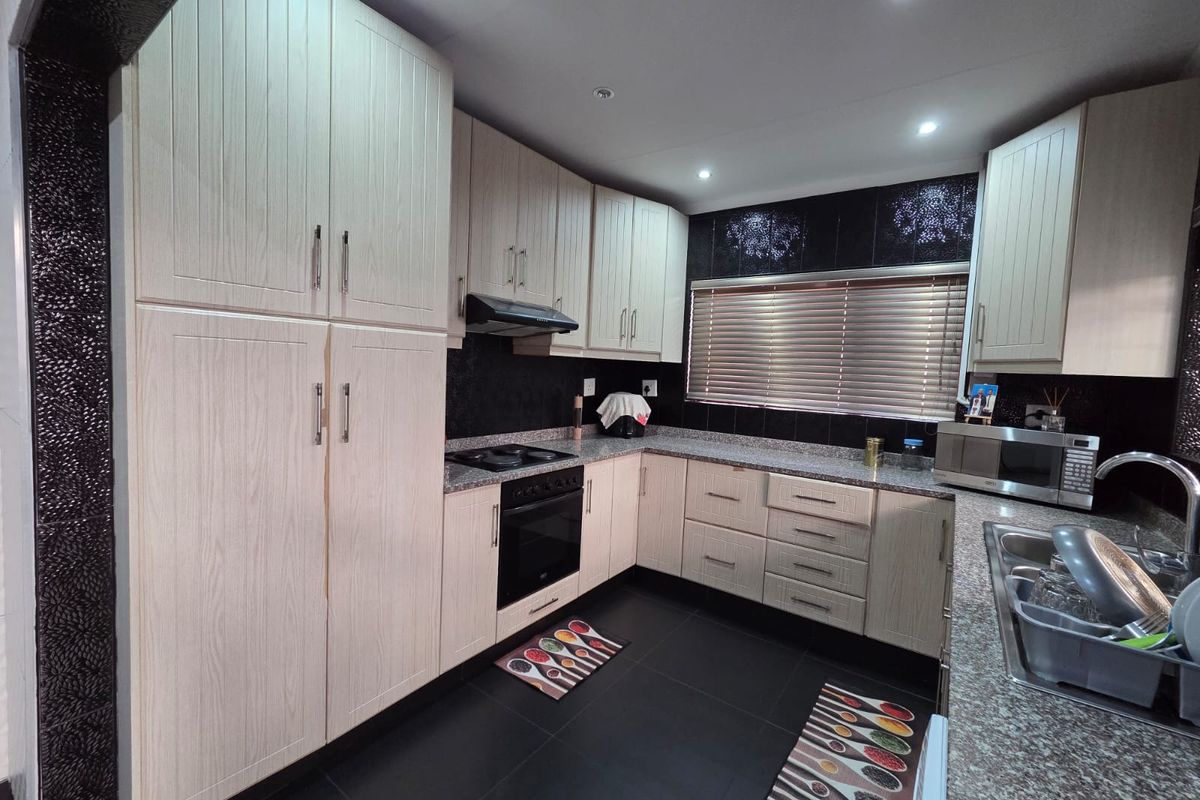 Modern kitchen featuring light wood-grain cabinetry, granite countertops, black tiled splashbacks, and integrated appliances, offering a functional and contemporary cooking space.