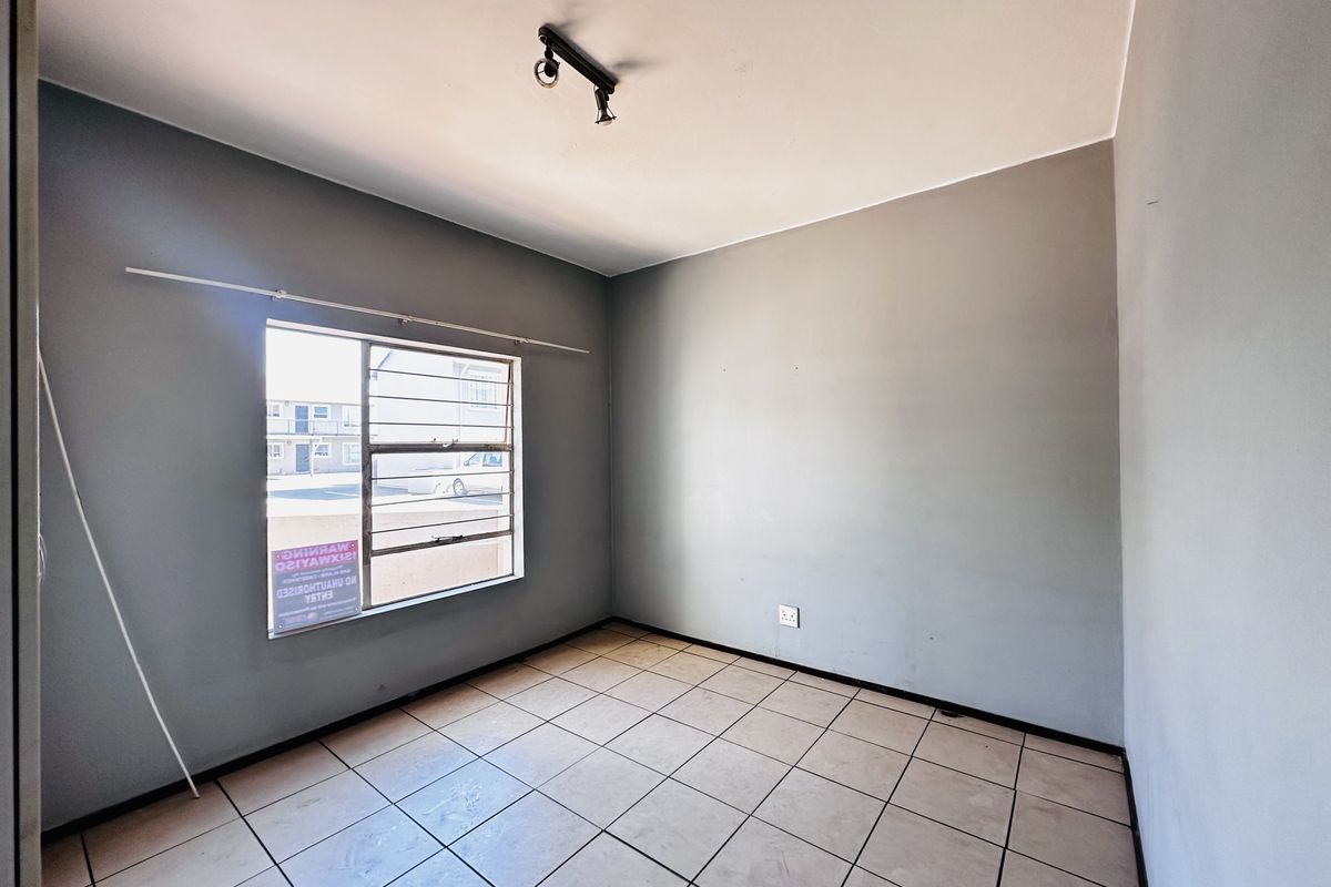 A vacant bedroom featuring neutral grey walls, tiled flooring, and a window fitted with security bars.