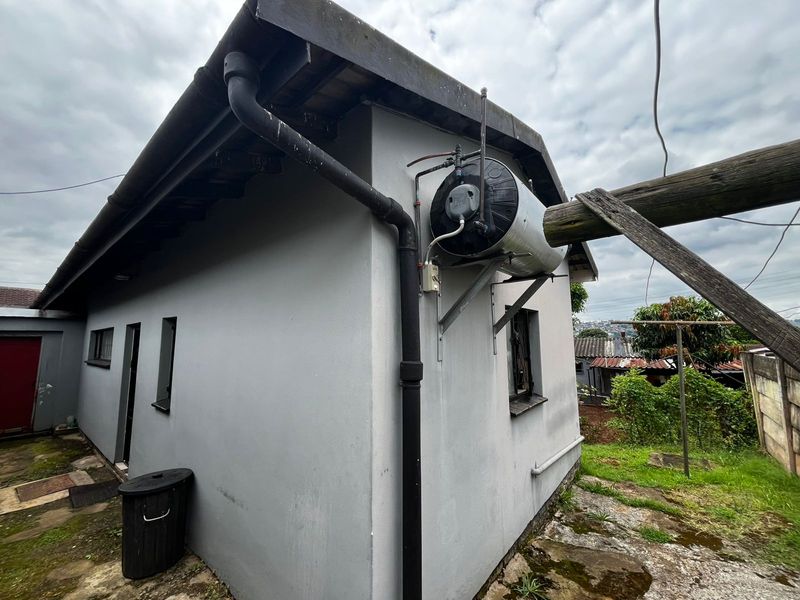 Rear exterior view of the property showing an externally mounted electric water heater, guttering, and concrete paving area.