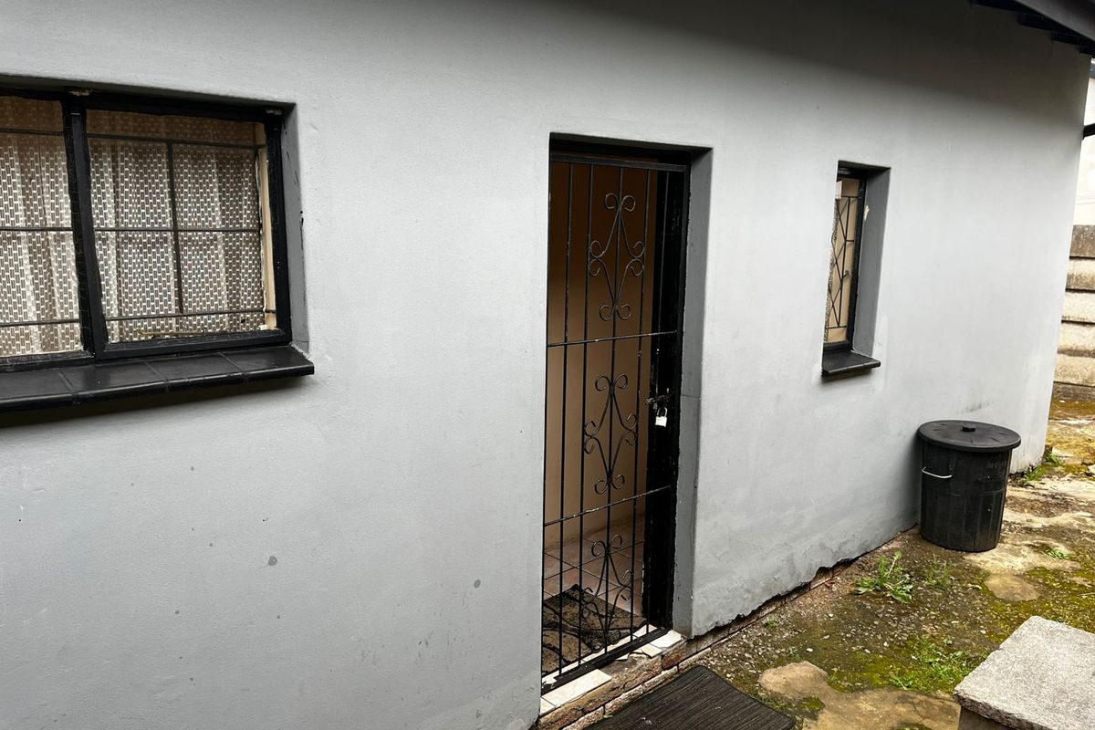 Rear exterior view of the property featuring grey painted walls, security gates, and barred windows with tiled sills.