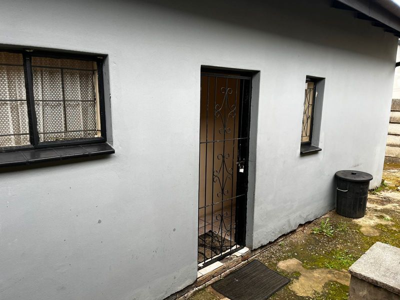 Rear exterior view of the property featuring grey painted walls, security gates, and barred windows with tiled sills.