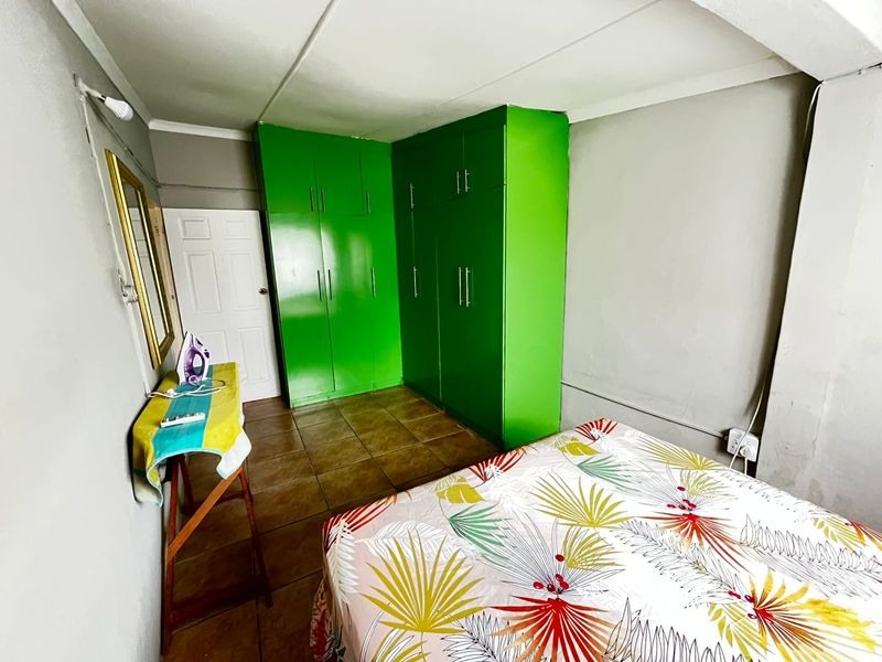 A bedroom featuring built-in green cabinetry, tiled flooring, and a standard panel door, requiring cosmetic updates to improve the overall finish.