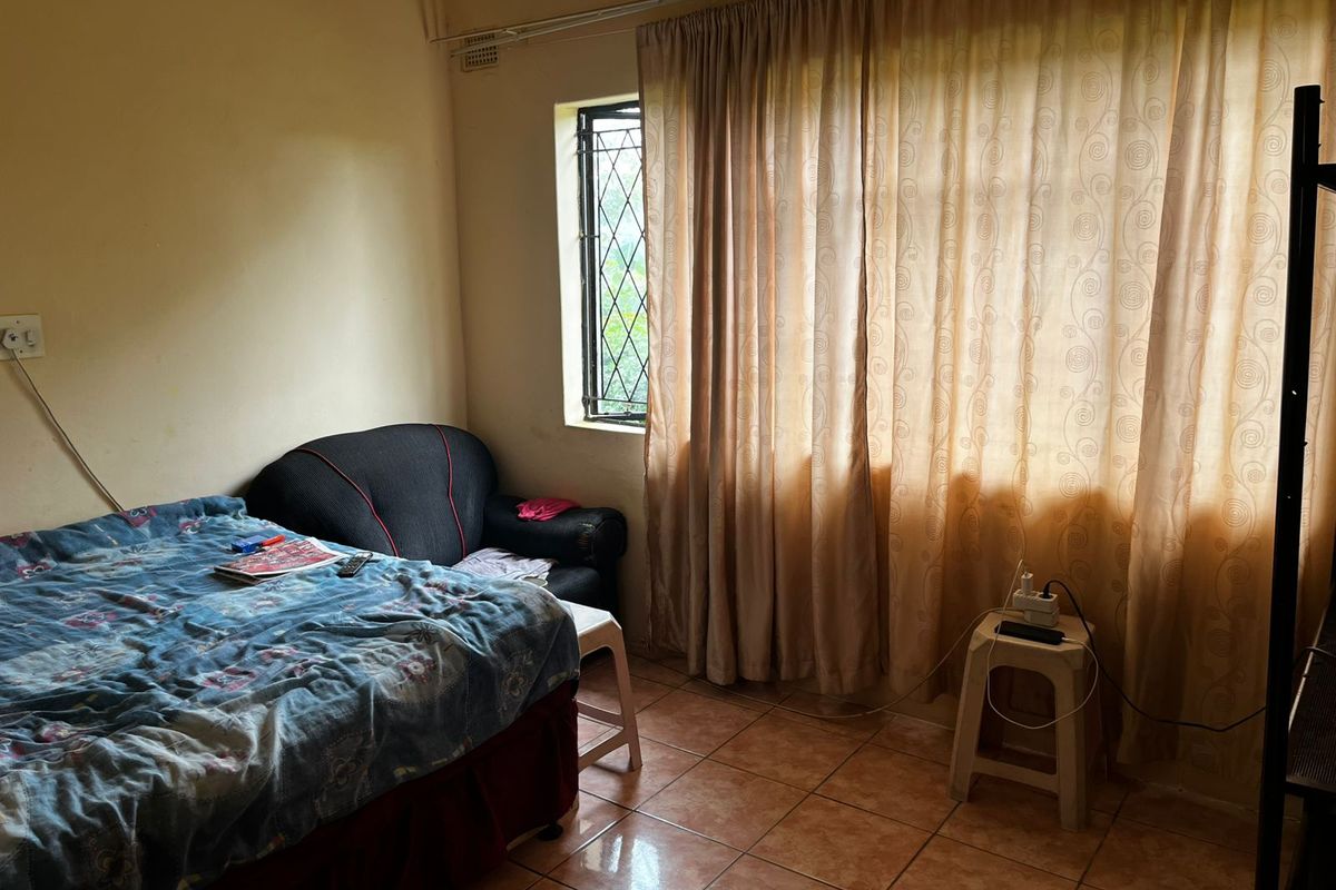 A bedroom featuring tiled flooring and a window with security bars, requiring cosmetic updates to improve the overall aesthetic and condition.