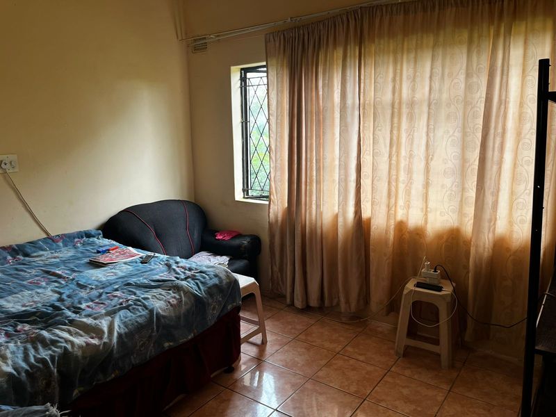 A bedroom featuring tiled flooring and a window with security bars, requiring cosmetic updates to improve the overall aesthetic and condition.
