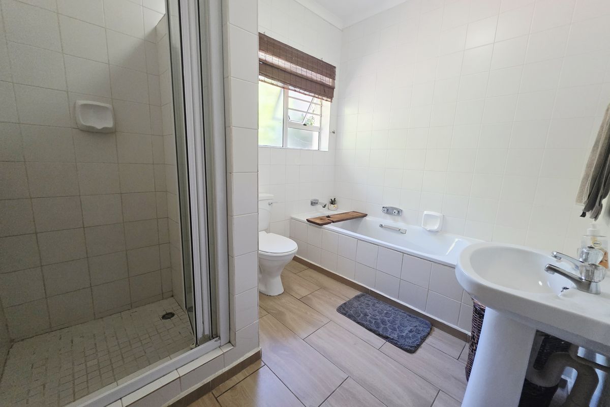 A clean, functional bathroom featuring a separate shower enclosure, built-in bathtub, pedestal basin, and neutral wall and floor tiling.