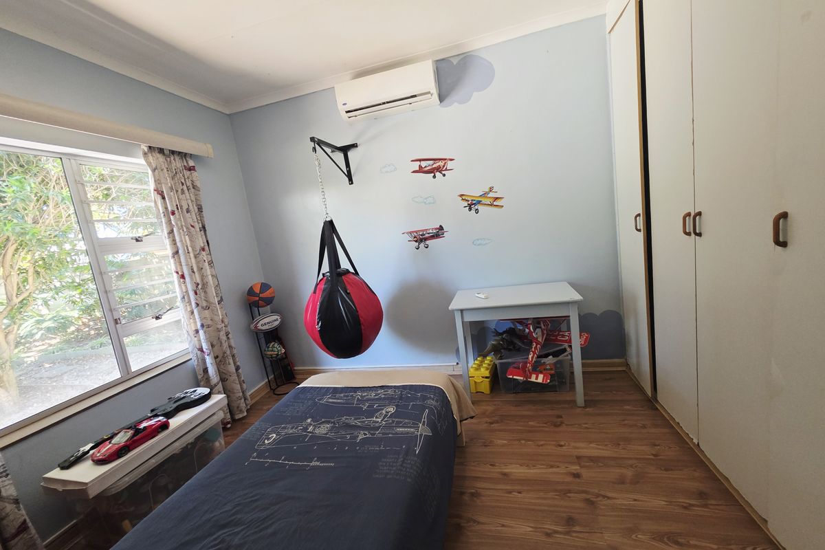 A bedroom featuring laminate flooring, built-in cupboards, and a wall-mounted split-system air conditioner.