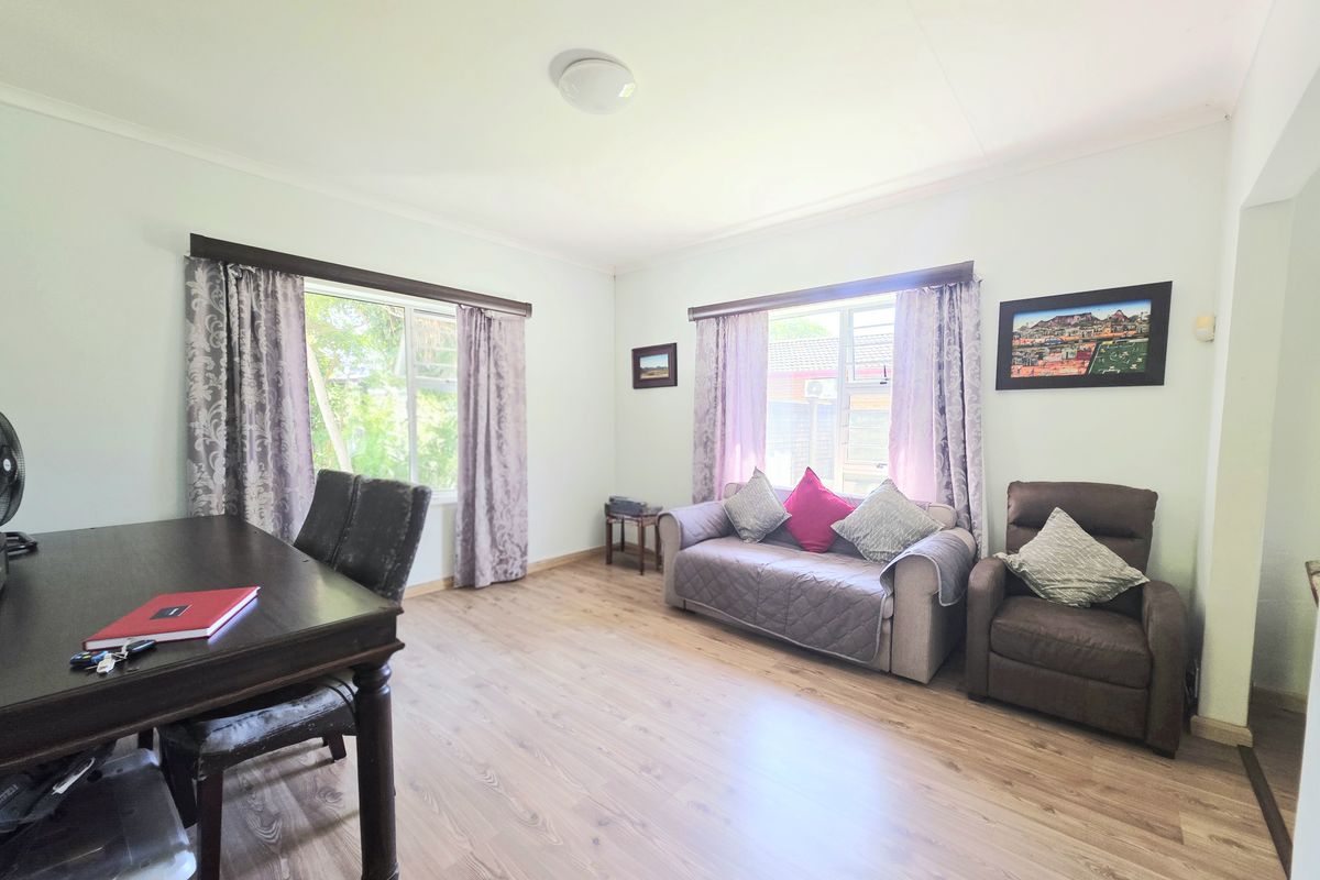 A bright living room featuring light-toned laminate flooring and large windows with natural light, offering a neutral canvas for interior updates.