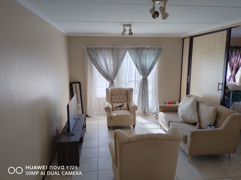 A living room featuring tiled flooring, built-in sliding door wardrobes, and ceiling-mounted spotlights, offering a functional and neutral living space.