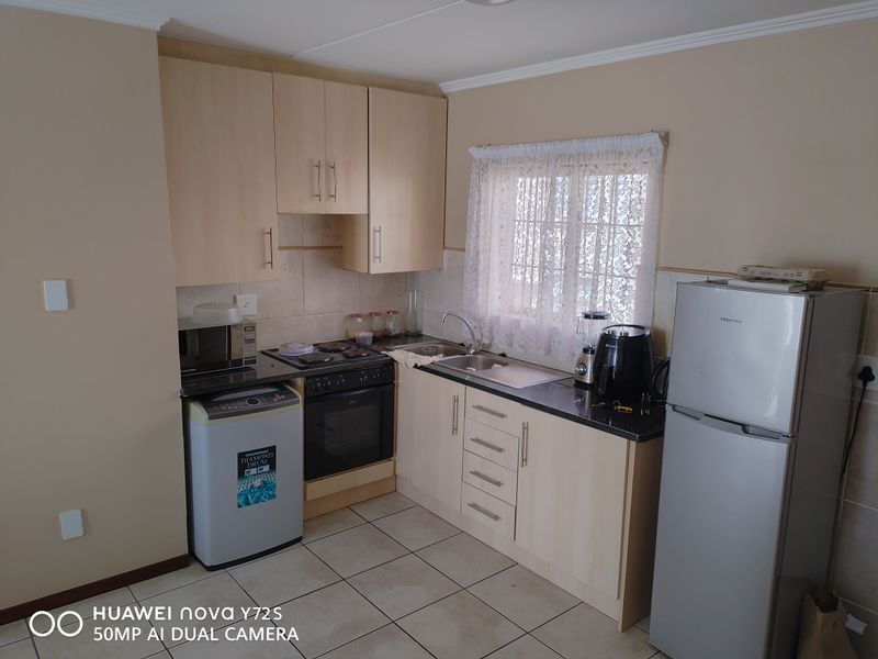 A functional kitchen featuring light wood-tone cabinetry, laminate countertops, tiled backsplash, and integrated electric stove and oven with tiled flooring.