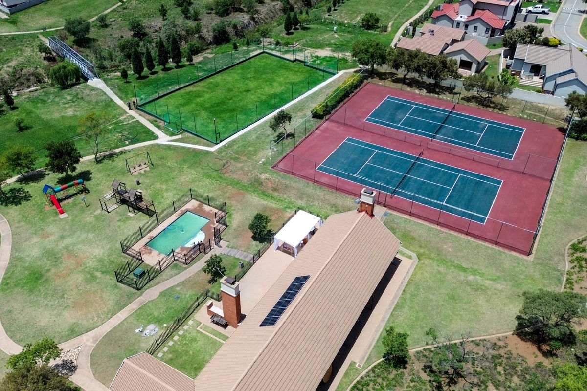 Aerial view of the estate clubhouse featuring tennis courts, a swimming pool, playground, and landscaped grounds with solar panels installed on the roof.
