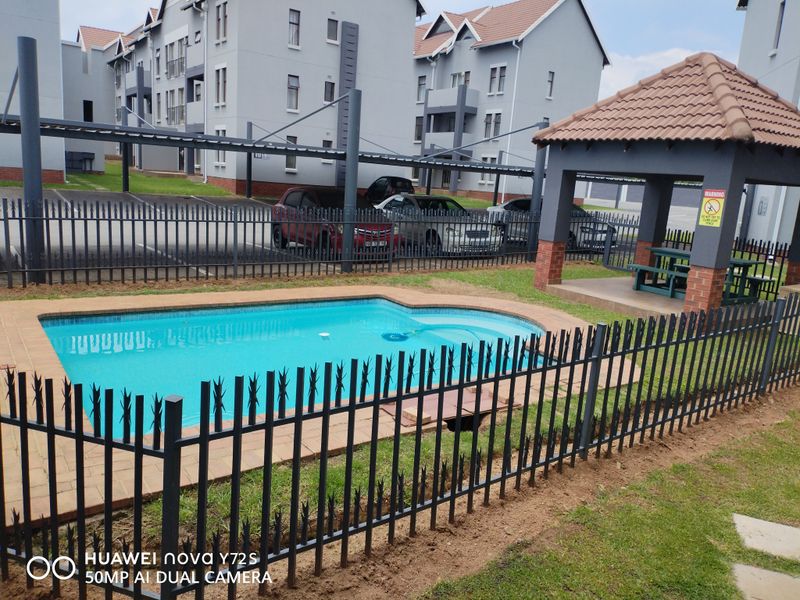 Communal pool area featuring a swimming pool, paved surround, and a covered gazebo within a secure apartment complex setting.