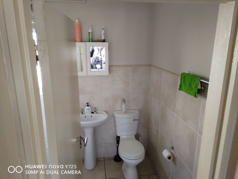 A compact bathroom featuring a pedestal basin, toilet, and wall-mounted medicine cabinet with neutral wall and floor tiling.