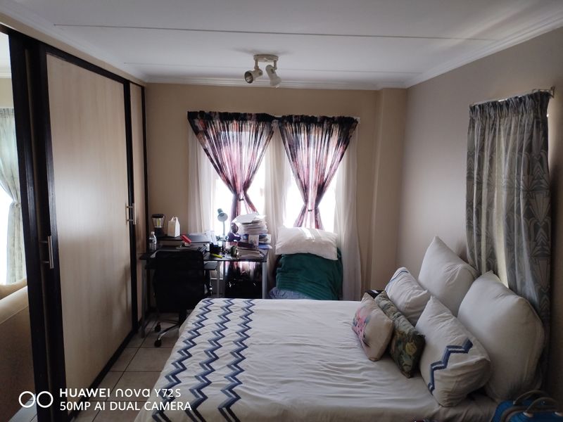 A bedroom featuring built-in wardrobes, tiled flooring, and ceiling-mounted lighting, offering a functional space with potential for modern updates.
