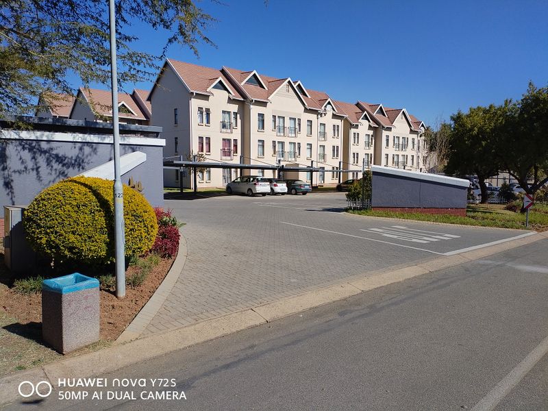 Exterior view of a multi-story apartment complex featuring a paved driveway, covered parking bays, and well-maintained landscaped grounds.