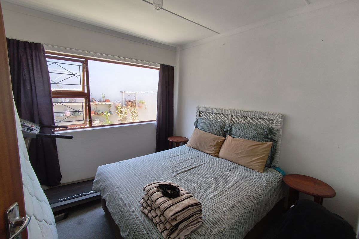 A standard bedroom featuring a large window with security bars, neutral walls, and a ceiling light fixture.