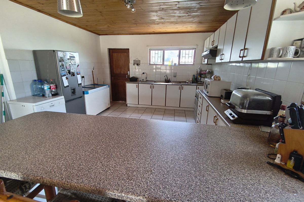 A functional kitchen featuring timber ceilings, tiled flooring, ample cabinetry, and a breakfast bar, offering a dated but practical layout for renovation.