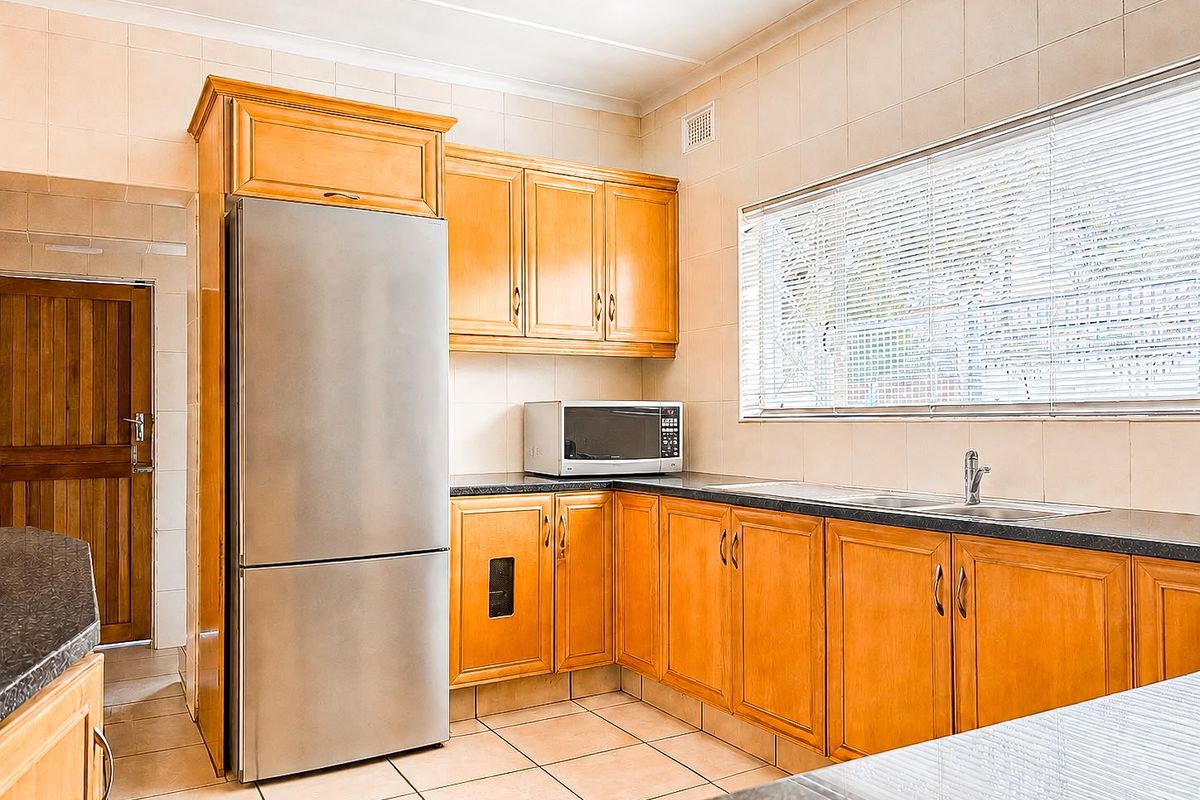A functional kitchen featuring wooden cabinetry, dark laminate countertops, tiled flooring, and a stainless steel sink with a window view.