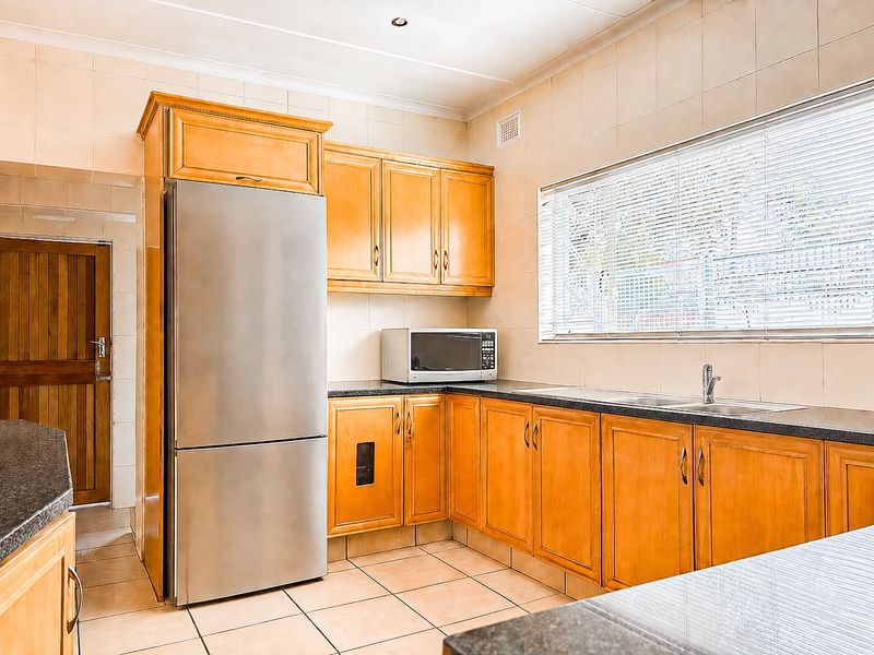 A functional kitchen featuring wooden cabinetry, dark laminate countertops, tiled flooring, and a stainless steel sink with a window view.