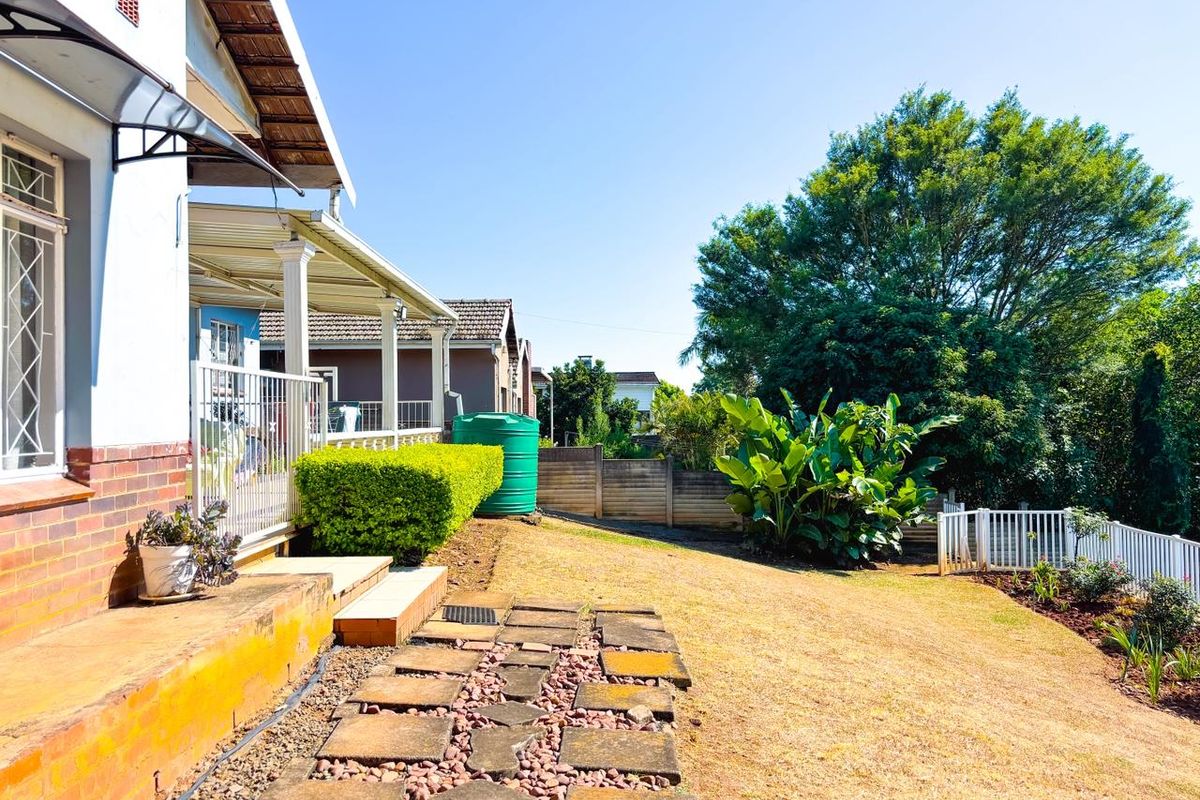 Rear exterior view featuring a covered patio, paved walkway, water tank, and a landscaped garden with boundary walling.