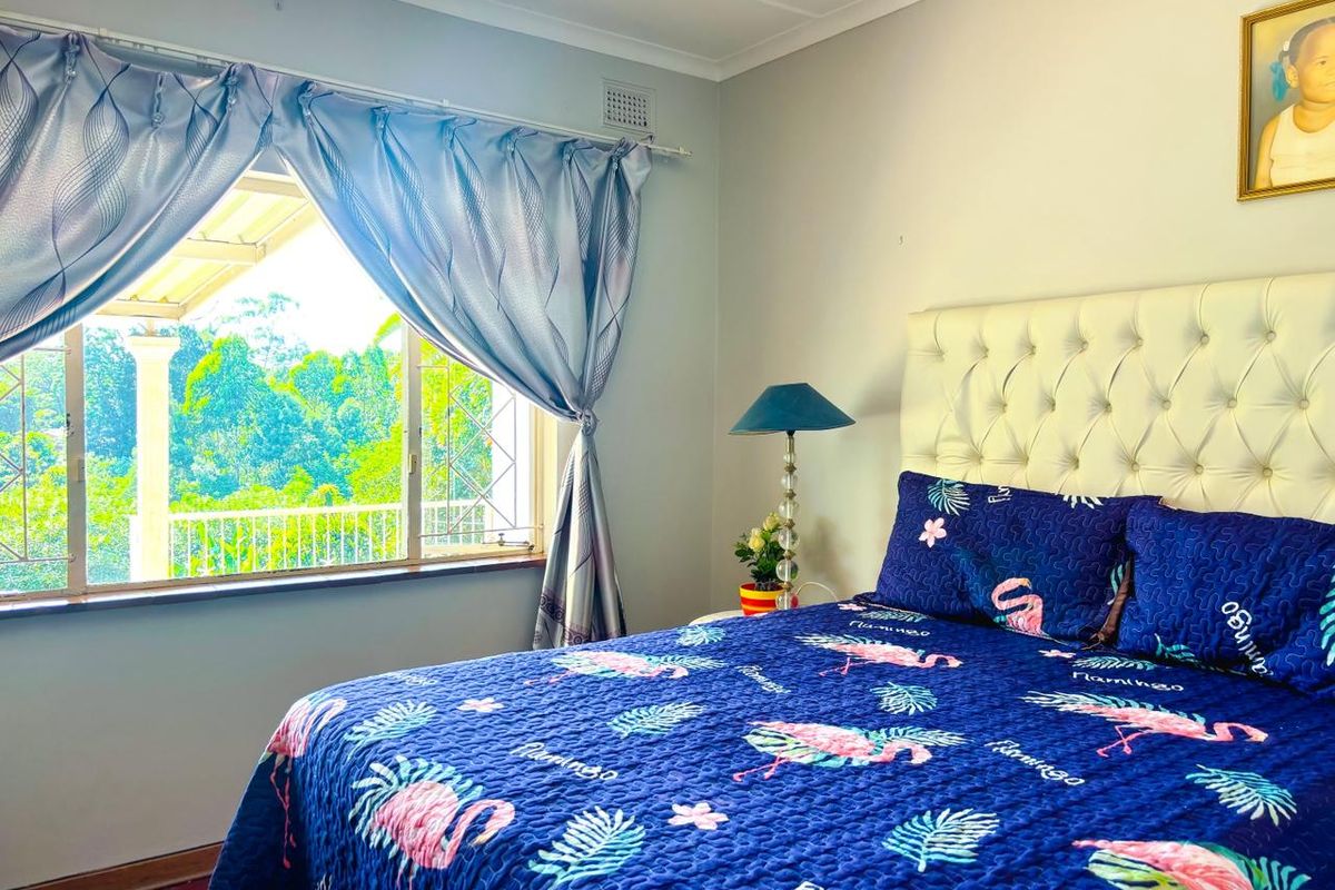 A bedroom featuring a large window with security bars, coving, and a ventilation grille, offering a pleasant view of the surrounding greenery.